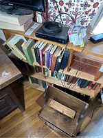 Books on wooden shelves with a black electronic device on top and a coiled cable, some books thick hardbacks, some paperbacks with worn spines.