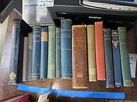 Top down view of 12 vintage books with cloth and paper bindings in various colors on wooden surface.