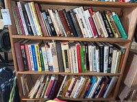Three shelves filled with assorted hardback and paperback books on various topics.