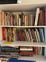 Three shelves filled with assorted hardback and paperback books of various subjects including sports and science.