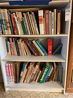 Shelf of assorted books with a prominent collection related to tennis including encyclopedias and instructional manuals; some books are stacked horizontally.