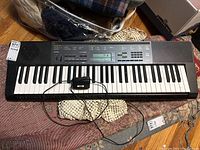 Full view of Casio CTK-5000 keyboard on patterned textile surface with power adapter connected.