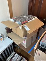Two cardboard boxes filled with numerous music CDs in jewel cases on a table.