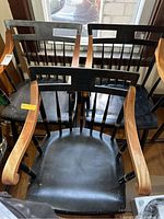 Front view of all three wooden arm chairs grouped together, showing black painted seats and backs with carved emblem and natural finish armrests