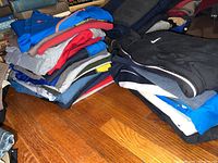 Two stacked piles of assorted fitness clothing in various colors including black, blue, gray, and red on a wood floor with background bookshelves visible.