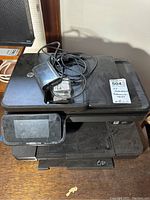 Front view of the HP Photosmart 7520 printer with power adapter and cables on top, showing touchscreen and paper tray.