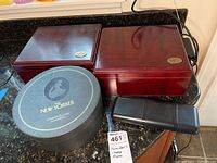 Photo showing two wooden humidors, round New Yorker cheese plate container, and black cigar holder on countertop.