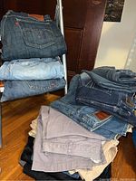 Stack of jeans folded on a chair and surface, various colors from dark denim to beige and black.