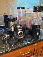 Photo showing multiple blender bases and plastic blender cups/canisters with lids on a counter