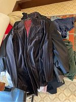 Pile of men's jackets and clothing on floor including a pinstripe blazer and dark solid jackets.