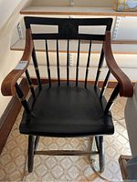 Front view of the black painted wooden armchair, showing curved arms and backrest with vertical spindles and emblem.