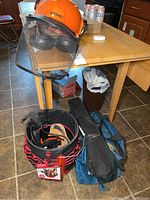 Photo showing Stihl safety helmet with attached mesh visor and hearing protection sitting on a table. Also visible are Husky tool bucket and tool bags on floor next to table.