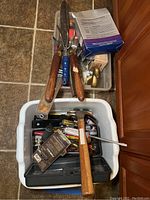Two bins containing assorted hand tools, gardening shears, brass duck, hooks, hammer, saw, axe, screwdrivers, and pliers as seen from above.