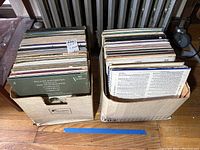 Top view of two cardboard boxes filled with vinyl records in sleeves, showing various album covers and spines