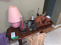 Tables with pink lamp, wooden elephant figurines, various candle holders and glass decorative items arranged on wooden table surface.