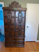 Full front view of the wooden armoire showing two doors with detailed carving and two drawers below.