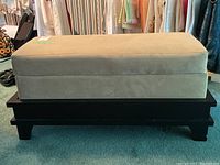 Front view of rectangular bedding box with beige faux suede top and black wooden base, showing side and legs.