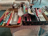 Wide view of two wicker baskets on a table, filled with assorted colored taper candles and metal candle holders.