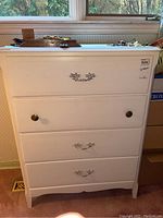 Front view of white wooden dresser showing decorative metal and knob drawer pulls