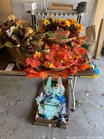 Artificial fall wreaths with leaves and sunflowers placed on table along with box containing glow-in-the-dark skeleton decorations.