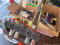 Photo showing a metal hardware component with multiple circular openings alongside boxes with assorted hardware items.