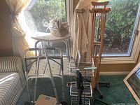 Photo showing bath seat, metal folding walker, and two wooden crutches standing against window and sofa.