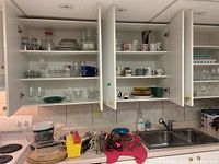 View of kitchen upper cabinets open showing shelves with various cups, mugs, plates, glasses, and bowls