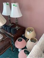 Two matching metal base lamps with white shades on a wooden side table, four various fabric lamp shades nearby.