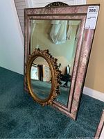 Photo showing the group of three mirrors: large square mirror with pink floral patterned frame and two smaller ornate oval gold-tone mirrors leaning against it