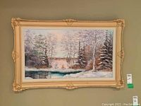 Frontal view of the framed oil painting depicting a snowy winter landscape with trees and a body of water, showing the full artwork and frame.