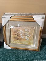 Five stacked framed prints of floral artwork with protective corner guards on gold frames, displayed on carpet
