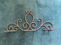 Ornate decorative metal wall mount with symmetrical curved scrolls lying on carpet.