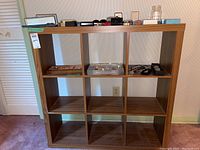 Front view of faux wood shelving unit showing nine open cubed compartments, medium brown wood grain finish.