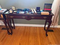 Full view of wooden side table showing two drawers and curved legs with various small items on top, which are not included in sale
