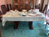 Photo of full dining table set up with white tablecloth and various dishes on top, showing table legs and room context.