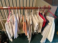 Multiple tablecloths hung on a wooden rod showing different sizes, types and colors primarily white/cream with one red item