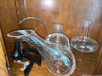 Three clear glass wine carafes displayed on a wooden shelf, two black plastic stands included