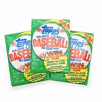 Photo showing front view of the three unopened 1984 Topps Major League Baseball card packs, green packaging with baseball and Topps logo prominently displayed.