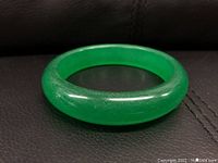 Green jade round bangle bracelet placed on dark surface to highlight color and shape.