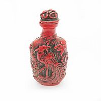 Front view of red cinnabar snuff bottle carved with peacock and floral designs.