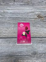 Front side of the BenchMark Strategic Metals .999 fine gold 1/4 grain bar in pink protective packaging on wooden surface.