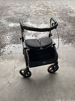 Black standing walker angled view showing padded seat, backrest, handles and front wheels