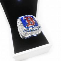Front view of the Boston Red Sox inspired championship ring showing the red 'B' logo, surrounded by clear rhinestones, set on a blue background with 'CHAMPIONS' engraved.