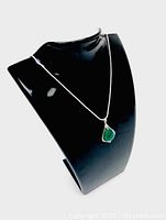 Green jade pendant on a black display stand showing the pendant shape and silver setting.