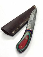 Full view of the hunting knife next to the brown leather sheath showing the colorful handle and Damascus steel blade pattern.