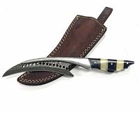 Damascus steel blade with curved shape and perforations alongside black and white striped handle next to brown leather sheath with stitching