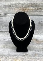 Double stranded black and white pearl necklaces displayed on a black mannequin bust against wooden background.