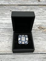 Front view of a ladies square-shaped ring in black jewelry box, showing blue enamel and clear semi-precious stones on silver-tone metal.