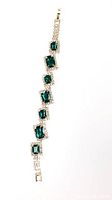 Full view of the gold-tone bracelet laid flat showing six square emerald green rhinestones each surrounded by smaller clear rhinestones with a gold-tone chain and clasp.