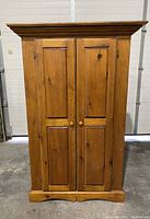 Front view of light brown wooden double door wardrobe with two paneled doors and round knobs.